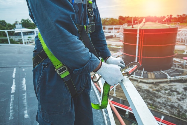 Travailleur masculin portant un harnais de sécurité d'abord et un seul de sécurité travaillant à un endroit de la main courante élevée sur l'huile de toit de réservoir à toit ouvert