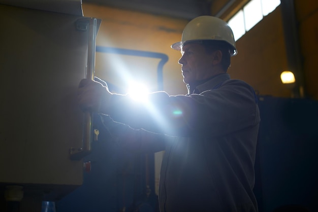 Travailleur masculin en salopette et casque presses sur le panneau de commande de l'équipement de l'usine