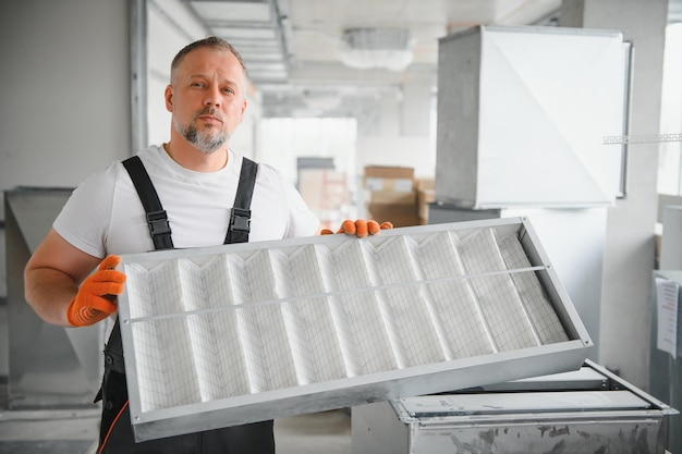 Un travailleur masculin tient un filtre à air pour la climatisation dans un bureau Installation d'un climatiseur