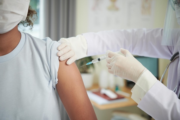 Travailleur médical dans des gants de protection injectant un vaccin contre le covid dans l'épaule d'une adolescente