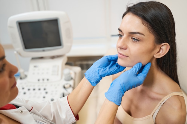 Travailleur médical professionnel debout devant son patient tout en faisant un bilan de la glande thyroïde