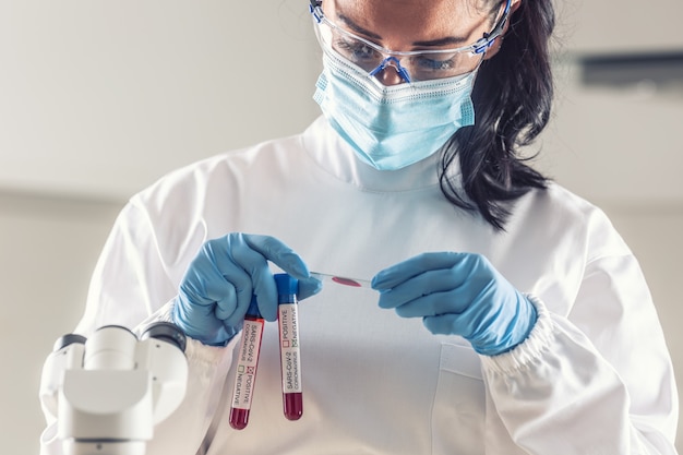 Un travailleur médical regarde un échantillon de sang sur une lame de microscope, tenant des ampoules d'échantillons positifs et négatifs de Covid-19.