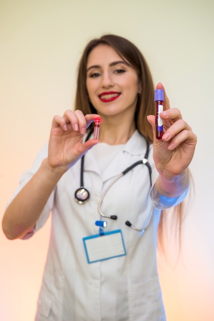 Travailleur médical avec des tubes à essai avec du sang pose en laboratoire. Belle femme en uniforme de protection