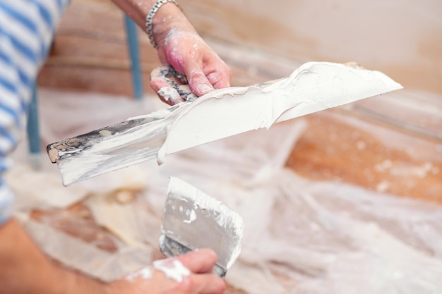 Un travailleur met du mastic sur une spatule pour enduire les murs intérieurs d'un salon