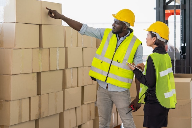 Un travailleur noir pointe vers une boîte en carton tandis qu'un jeune superviseur asiatique vérifie le document ensemble à l'usine de l'entrepôt