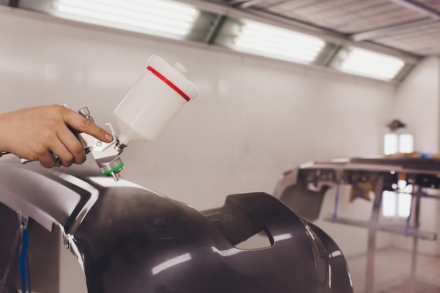 Travailleur peignant une voiture des pièces vierges noires dans un garage spécial, portant un costume et un équipement de protection.