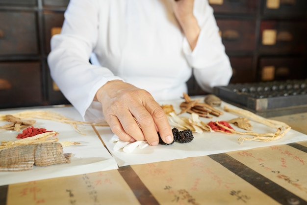 Travailleur de la pharmacie chinoise choisissant des baies et des champignons secs