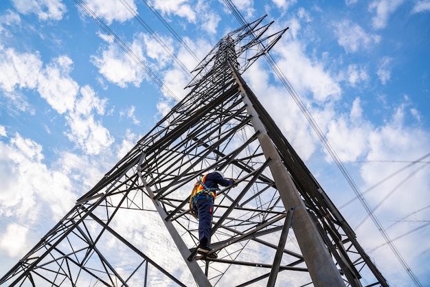 Un travailleur portant des combinaisons de sécurité grimpe sur des pylônes à haute tension pour entretenir des centrales électriques à haute tension