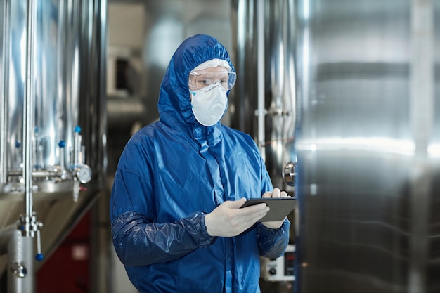 Travailleur portant un équipement de protection et un masque à l'aide d'une tablette dans une usine industrielle