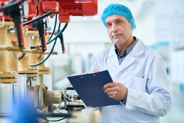 Travailleur posant par des tuyaux dans une usine moderne