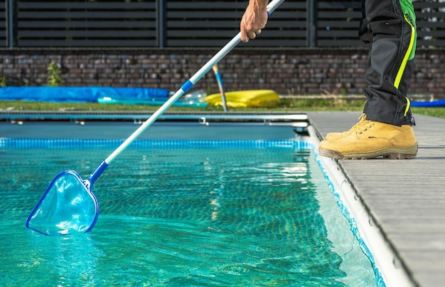 Photo travailleur professionnel caucasien de piscine avec un filet de piscine nettoyant une piscine extérieure résidentielle