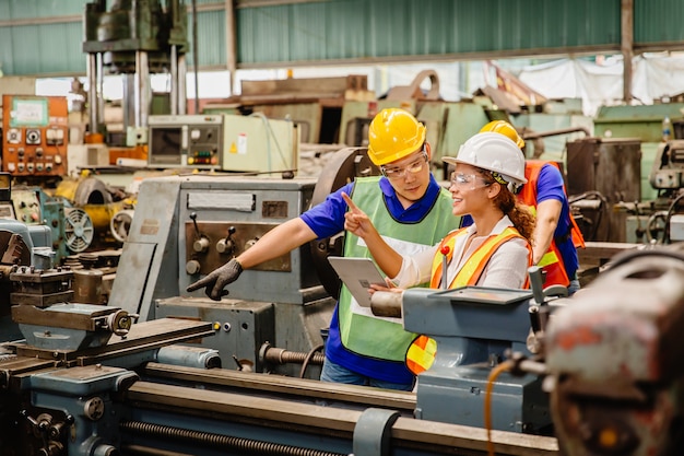 Travailleur de race mixte travaillant ensemble s'entraident pour travailler dans une machine de l'industrie lourde portant un costume de sécurité dans la chaîne de production en usine.ingénieur avec coworking sur tablette avec le personnel de l'équipe.