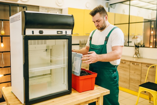 Travailleur avec réfrigérateur de réparation de boîte à outils à la maison