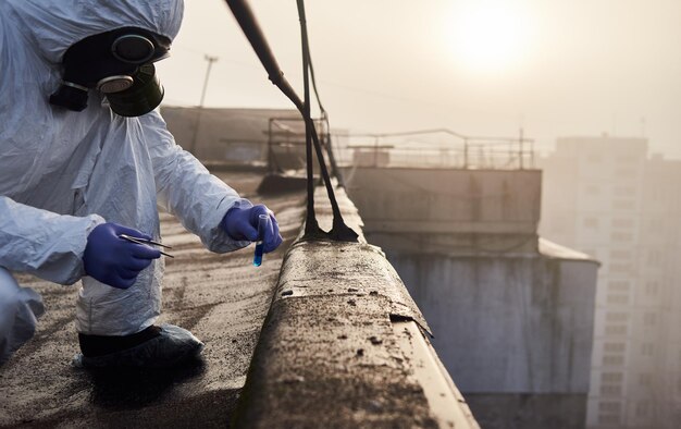 Travailleur scientifique portant une combinaison de protection et un masque à gaz faisant des tests écologiques sur le toit