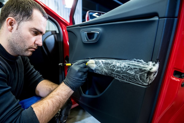 Le travailleur de service de voiture nettoie l'intérieur avec la brosse spéciale