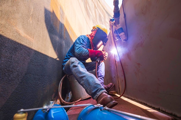 Travailleur de sexe masculin portant des vêtements de protection et réparant le soudage de la construction industrielle du pétrole et du gaz ou du réservoir de stockage à l'intérieur des espaces confinés