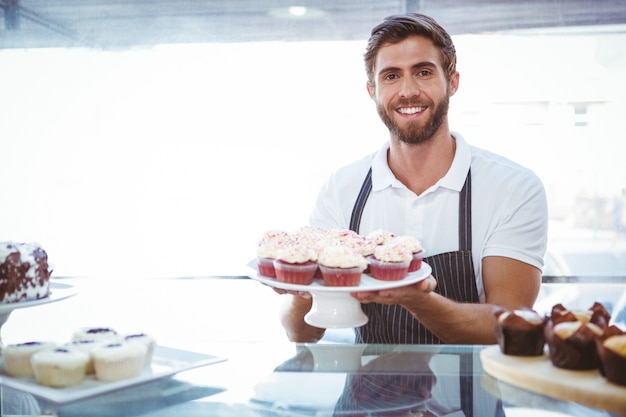 Travailleur souriant tenant des cupcakes derrière le comptoir