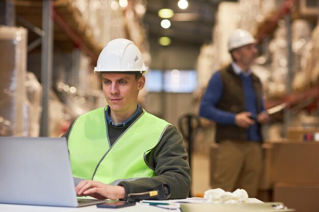 Travailleur souriant utilisant un ordinateur portable dans un système de distribution de gestion d'entrepôt