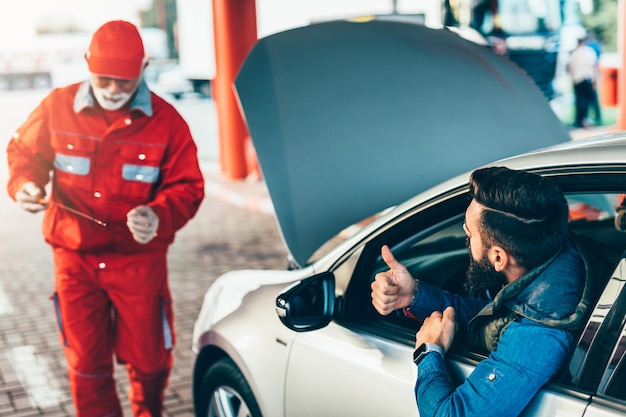 Travailleur supérieur debout sur une station-service, alimentant la voiture et vérifiant le niveau d'huile moteur.