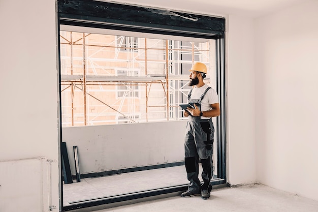 Un travailleur avec une tablette dans les mains vérifiant l'appartement en cours de construction