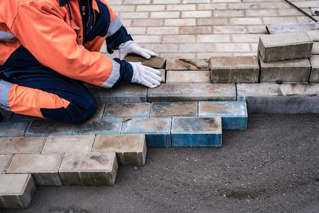 Un travailleur en tenue de travail protectrice pose des dalles de pavage Un professionnel