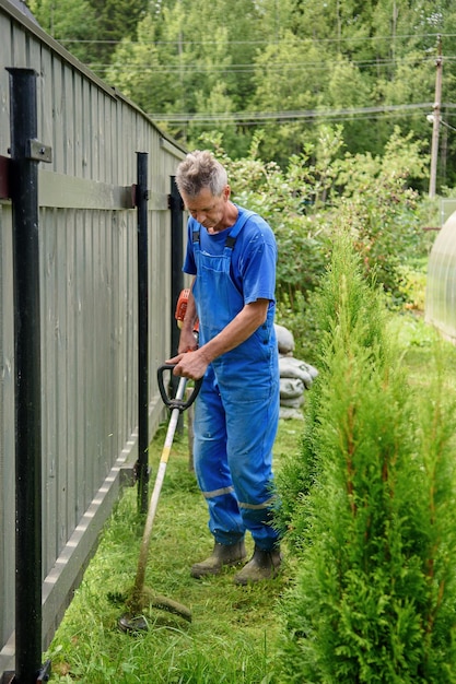 Travailleur avec une tondeuse à main dans ses mains tond l'herbe devant la maison La tondeuse est entre les mains d'un homme Le jardinier coupe l'herbe