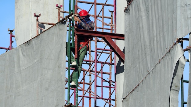 Travailleur travaillant sur un chantier de construction avec un casque et un équipement de sécurité et couvrant le bâtiment avec du vinyle de couleur grise et du ciel bleu.