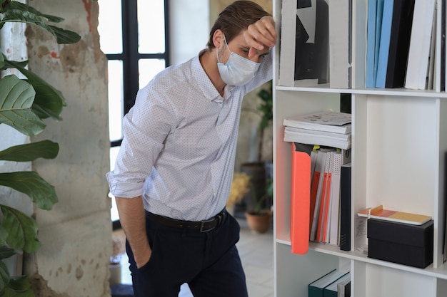 Travailleur triste en masque médical debout au bureau.