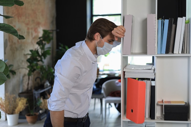 Travailleur triste en masque médical debout au bureau.