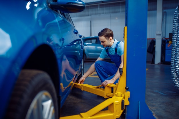 Travailleur en uniforme fixe véhicule sur ascenseur, service de voiture