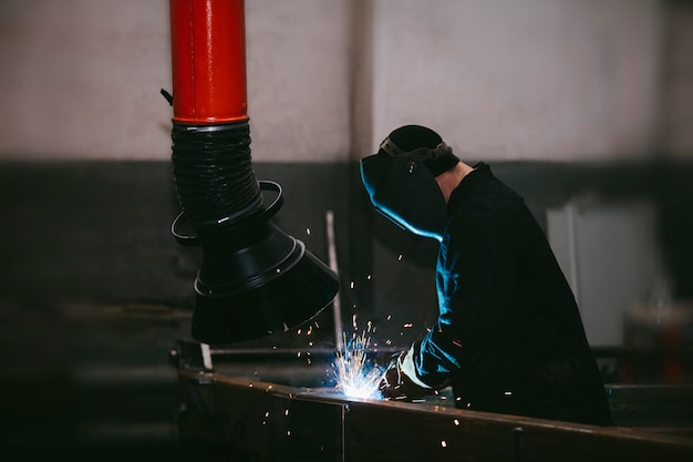 Travailleur à l'usine dans le casque est de fer dans le processus de soudage des étincelles lumineuses