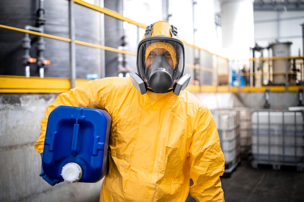 travailleur de l'usine de production de produits chimiques en tenue de protection et masque à gaz tenant une boîte en plastique avec un produit chimique