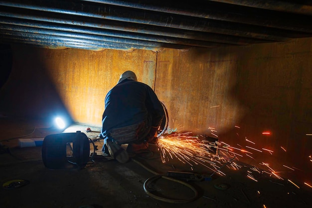 Travailleur utilisant une étincelle de roue électrique meulant du métal fait partie de la construction de tuyaux de poutre de réservoir de plaque de machines étincelle flash à l'intérieur confiné