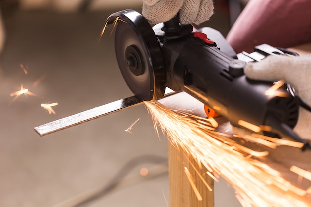 Travailleur utilisant une meuleuse d'angle en usine et jetant des étincelles.