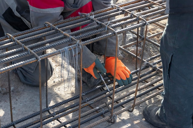 Un travailleur utilise du fil d'attache en acier pour fixer des tiges d'acier aux barres d'armature Gros plan Structures en béton armé tricotant une cage d'armature métallique