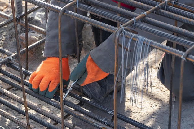 Un travailleur utilise du fil d'attache en acier pour fixer des tiges d'acier aux barres d'armature Gros plan Structures en béton armé tricotant une cage d'armature métallique