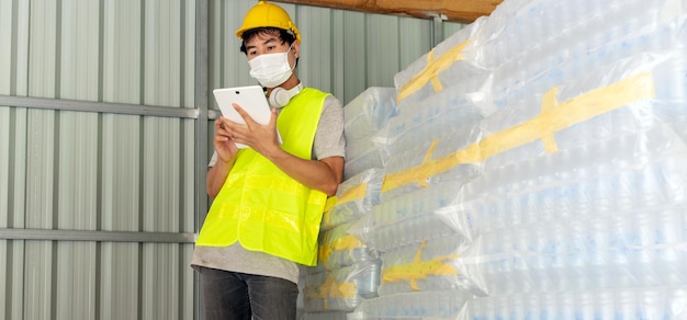 Un travailleur vérifiant le stock de bouteilles en plastique dans l'entrepôt Utilisant une tablette pour mettre à jour le stock en ligne