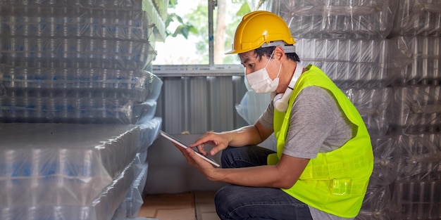 Un travailleur vérifiant le stock de bouteilles en plastique dans l'entrepôt Utilisant une tablette pour mettre à jour le stock en ligne