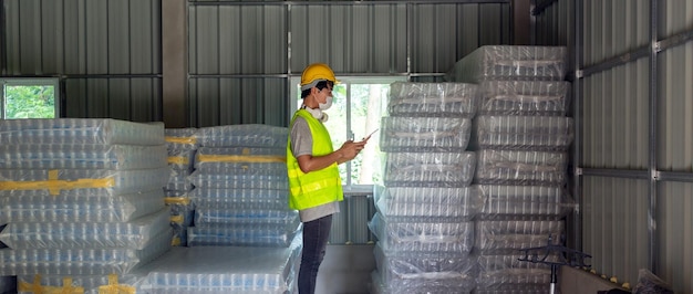 Un travailleur vérifiant le stock de bouteilles en plastique dans l'entrepôt Utilisant une tablette pour mettre à jour le stock en ligne