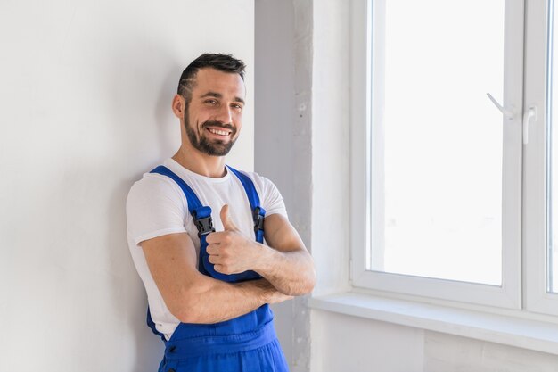 Un travailleur en vêtements de travail bleus se tient contre le mur et pose