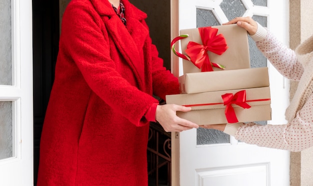 Photo travailleur vêtu d'un manteau rouge offrant des coffrets cadeaux près de la porte blanche