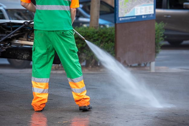 Travailleur de la ville avec un pistolet à pression d'eau. Nettoyage des rues et du mobilier urbain, pour la prévention du covid19, du coronavirus