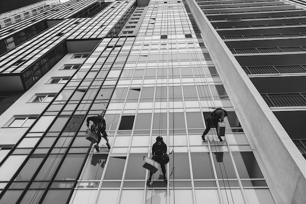 Les travailleurs de l'alpinisme industriel sont suspendus au-dessus du bâtiment de la façade résidentielle tout en lavant le vitrage de la façade extérieure. Les ouvriers d'accès de corde se bloque sur le mur de la maison. Concept de travaux urbains de l'industrie. Espace de copie