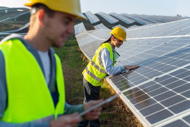 Travailleurs attentifs dans des gilets de signalisation et des casques de protection touchant le panneau solaire se penchant et vérifiant les dommages ou la déformation tout en travaillant à l'air libre