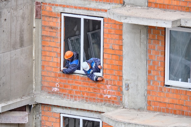 Les travailleurs d'un chantier de construction installent des fenêtres dans un immeuble résidentiel