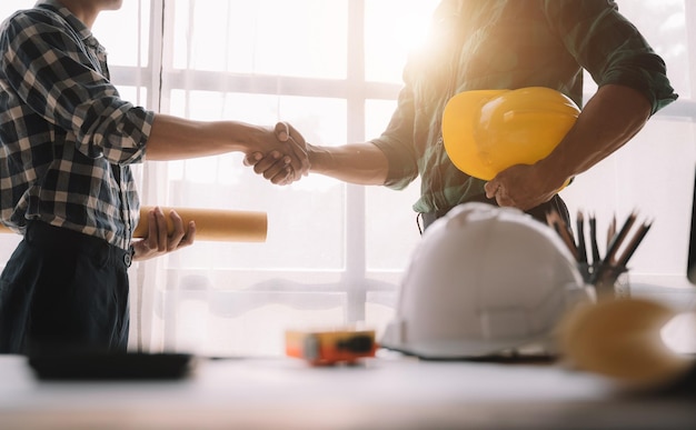 Travailleurs de la construction, architectes et ingénieurs se serrent la main tout en travaillant pour le travail d'équipe et la coopération après avoir conclu un accord dans un concept de coopération réussie dans un bureau