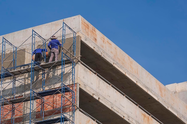 Travailleurs de la construction sur des échafaudages plâtrant un mur de ciment sur le toit du bâtiment du garage de stationnement