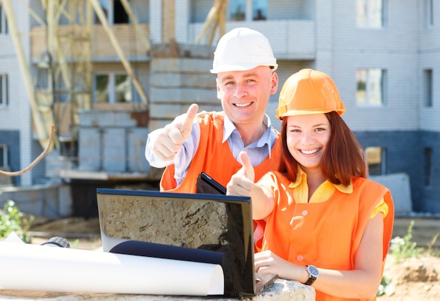 Travailleurs de la construction féminins et masculins de succès avec un ordinateur portable et des dessins