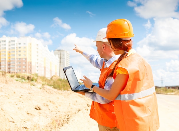 Travailleurs de la construction, femmes et hommes, regardant un ordinateur portable de maisons en construction