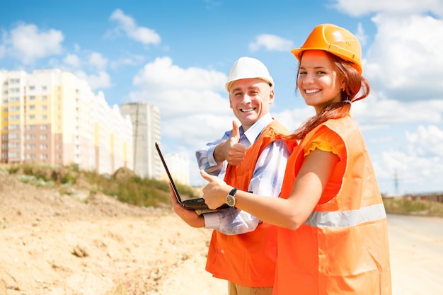 Travailleurs de la construction, femmes et hommes, regardant un ordinateur portable de maisons en construction